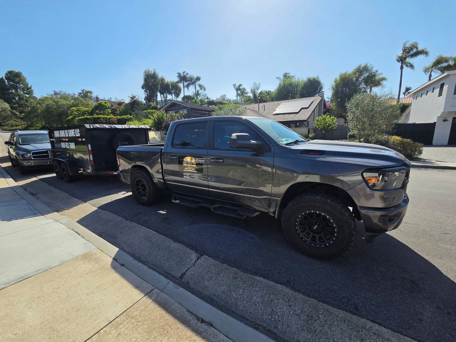 Black pickup truck parked on a sunny residential street beside a driveway and another truck