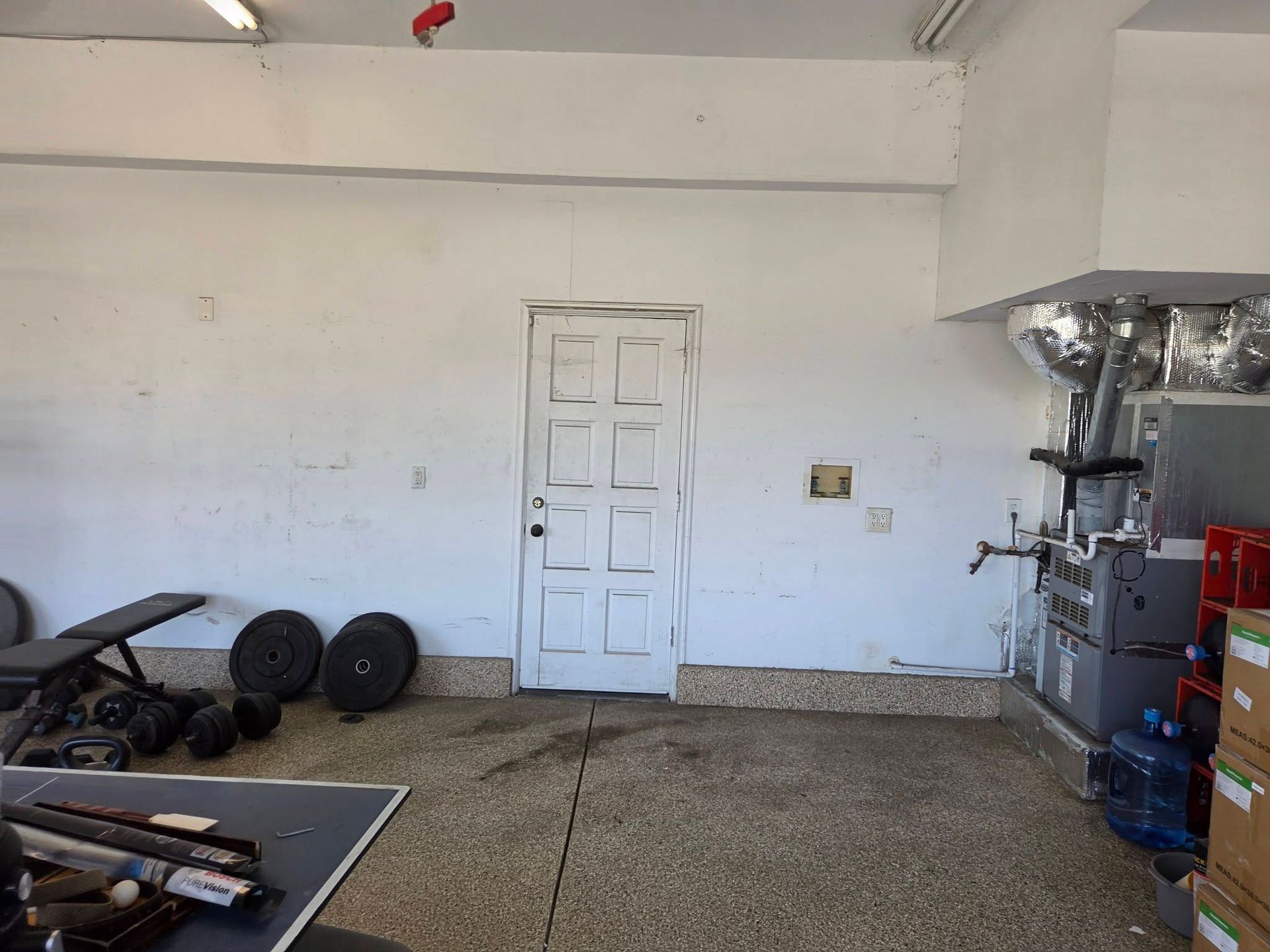 Empty garage with a white door, scattered equipment on the floor, and metal machinery along the right wall.