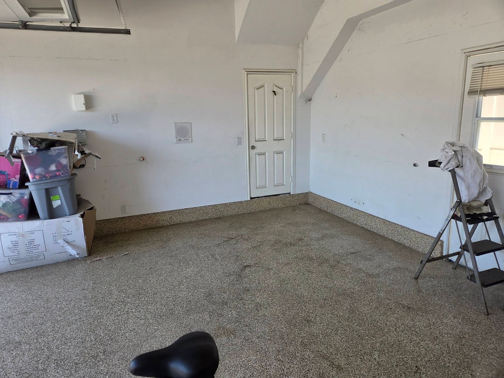 Empty garage interior with white walls, closed door, and storage items along the sides