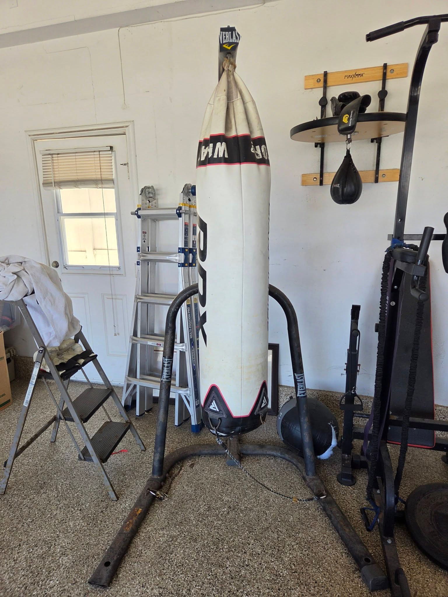 Home gym with a white heavy bag, exercise equipment, and storage shelves on a gravel floor