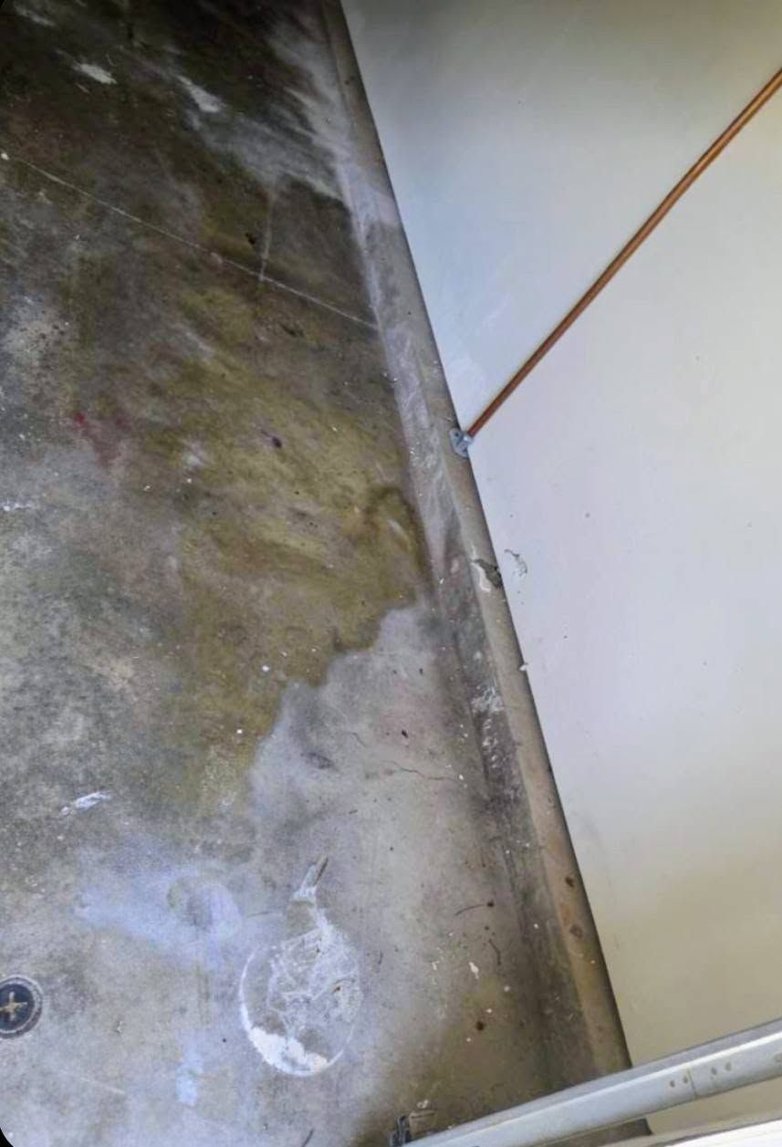 Cracked concrete floor beside a white wall with a metal pipe along the edge