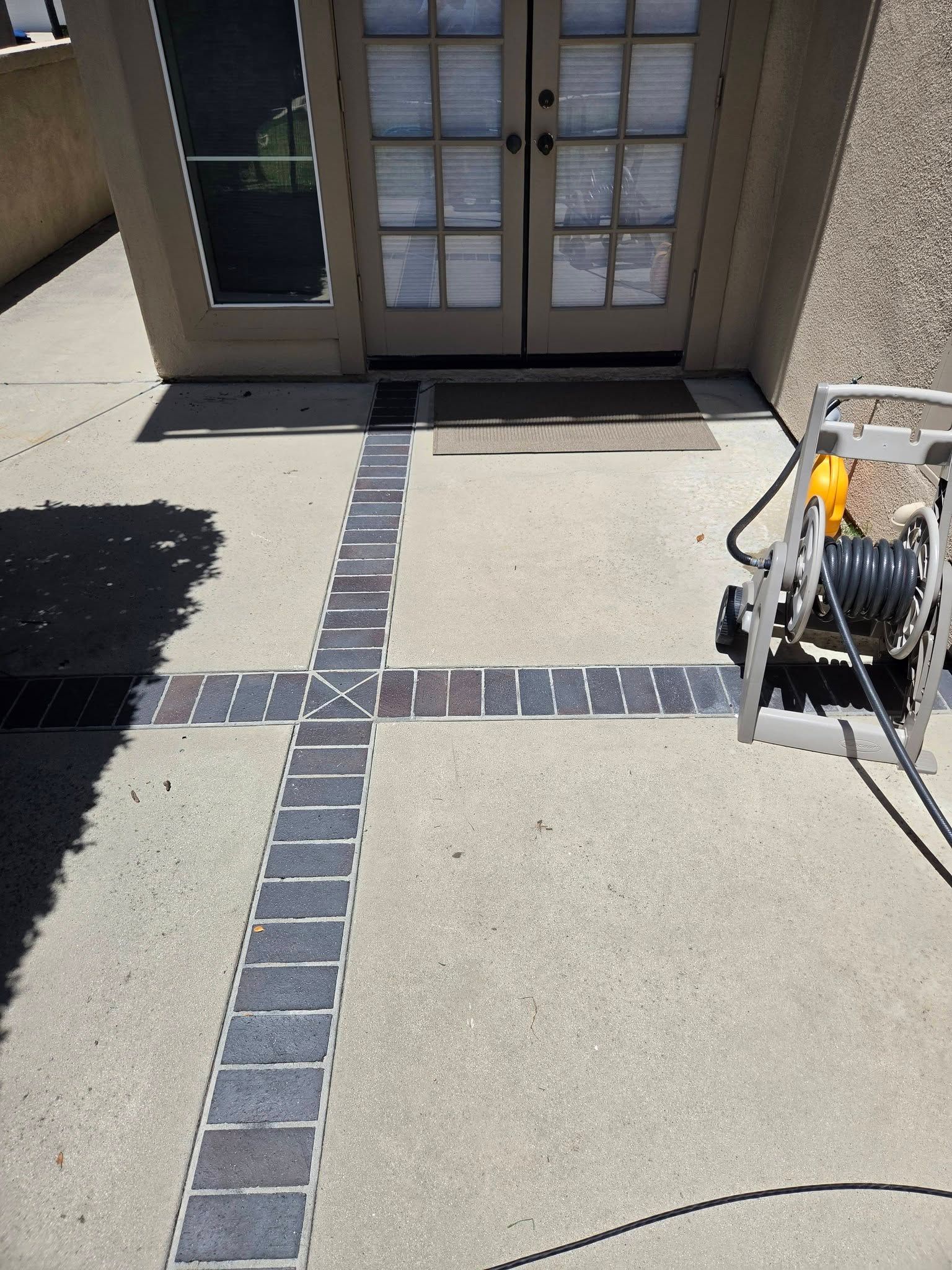 Front entrance with tactile paving cross, concrete walkway, and a hose reel on the right.