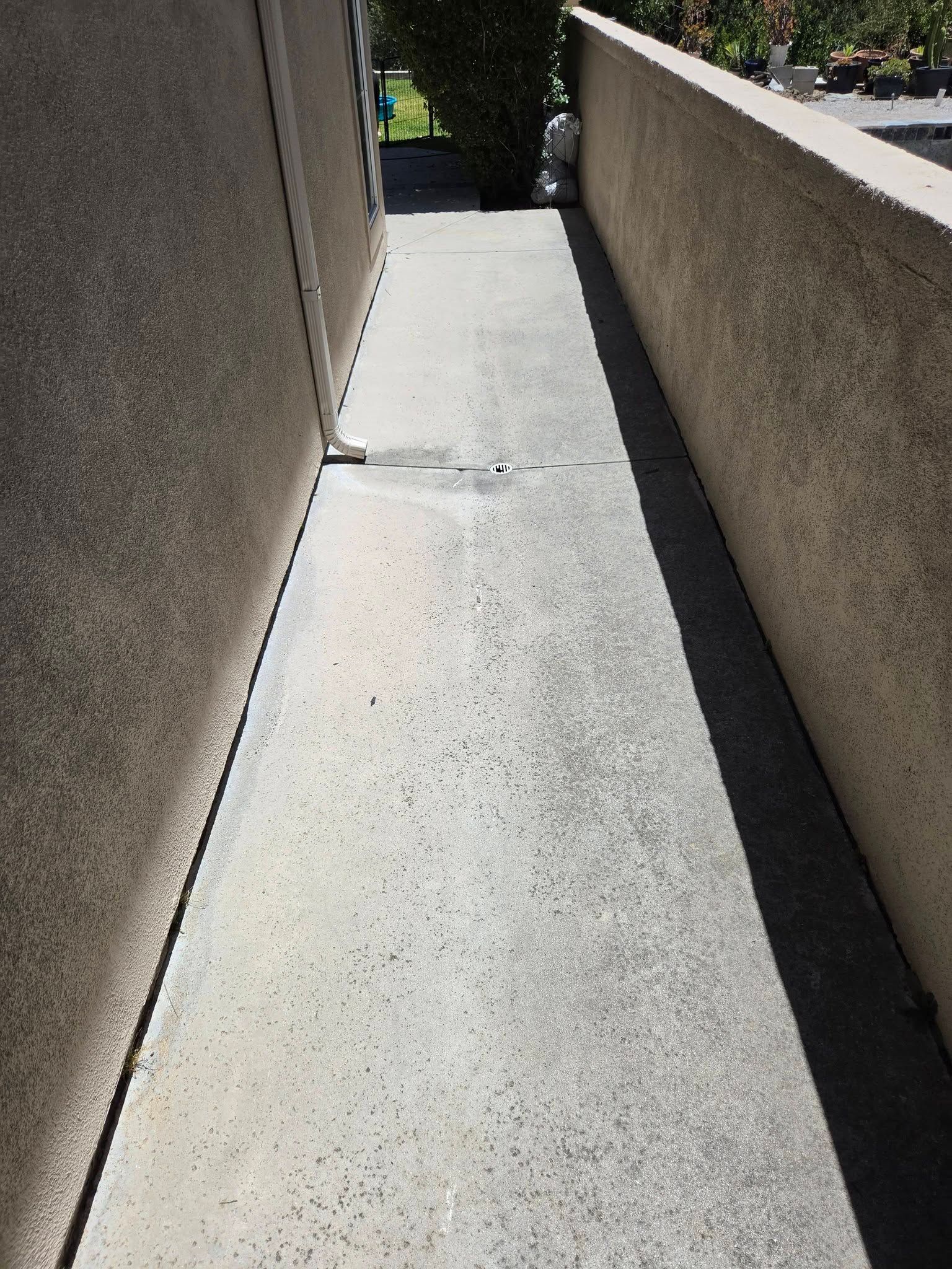 Narrow concrete walkway between beige walls in bright sunlight, sloping toward a darker opening ahead