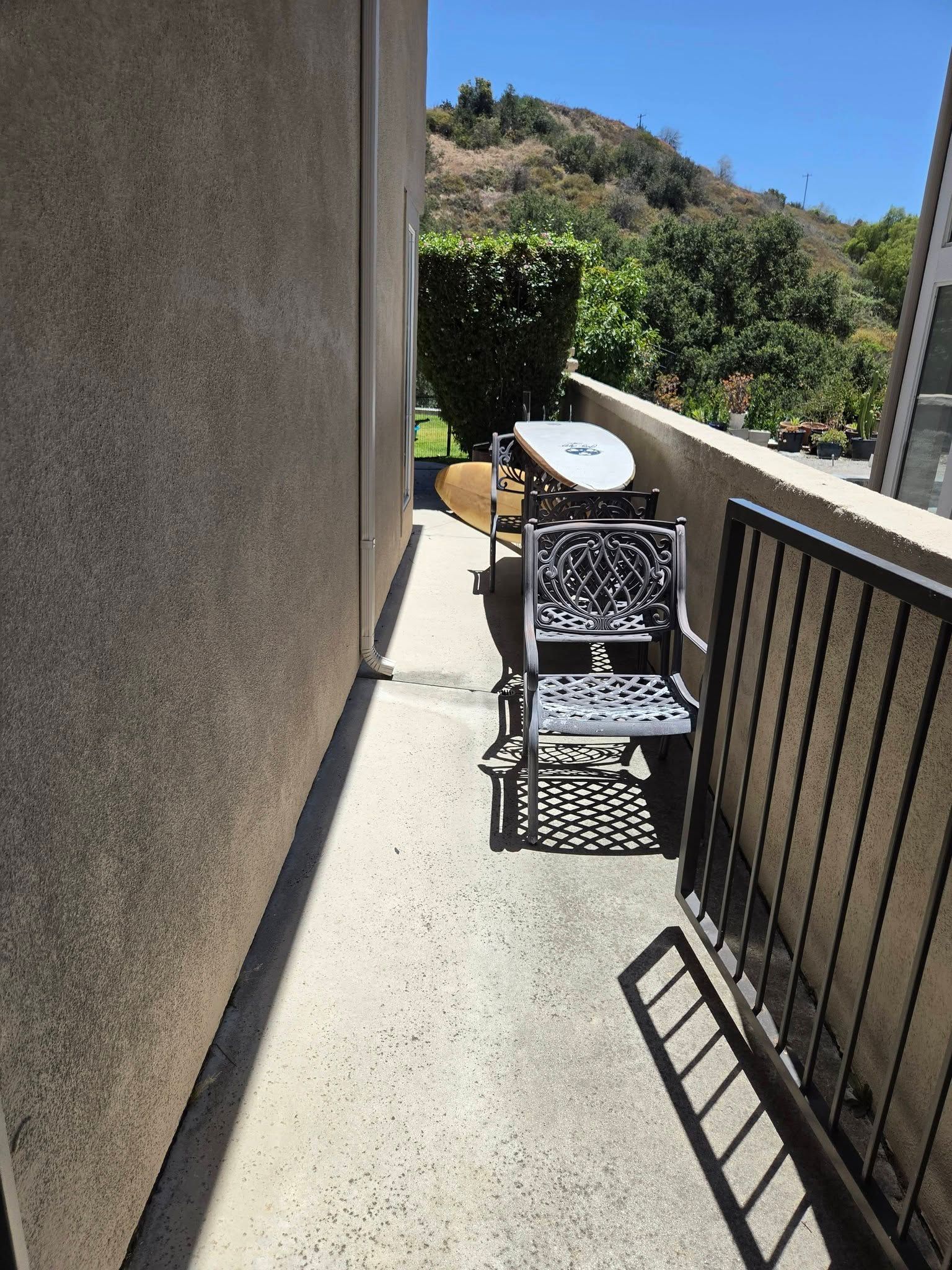Sunny outdoor patio with metal chairs and a small table beside a beige wall and railing.