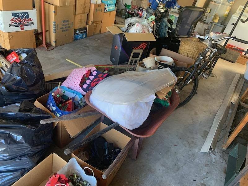 Cluttered garage with stacked boxes, bags, and a bicycle under a pile of miscellaneous items