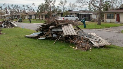 Collapsed roof debris on a grassy lawn after storm damage in a residential neighborhood