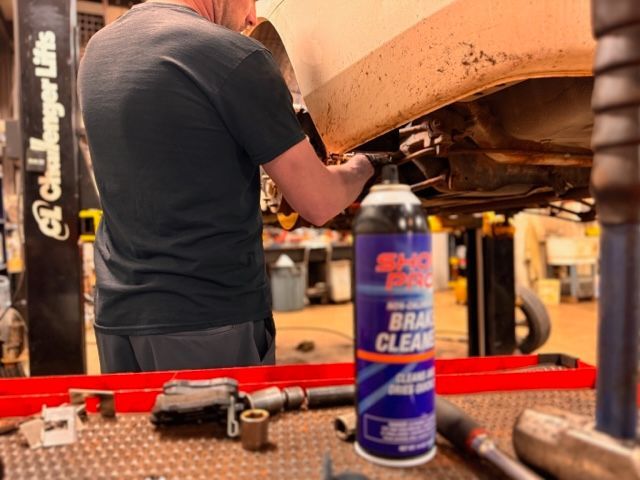 A man is working on a car in a garage next to a can of brake clean.