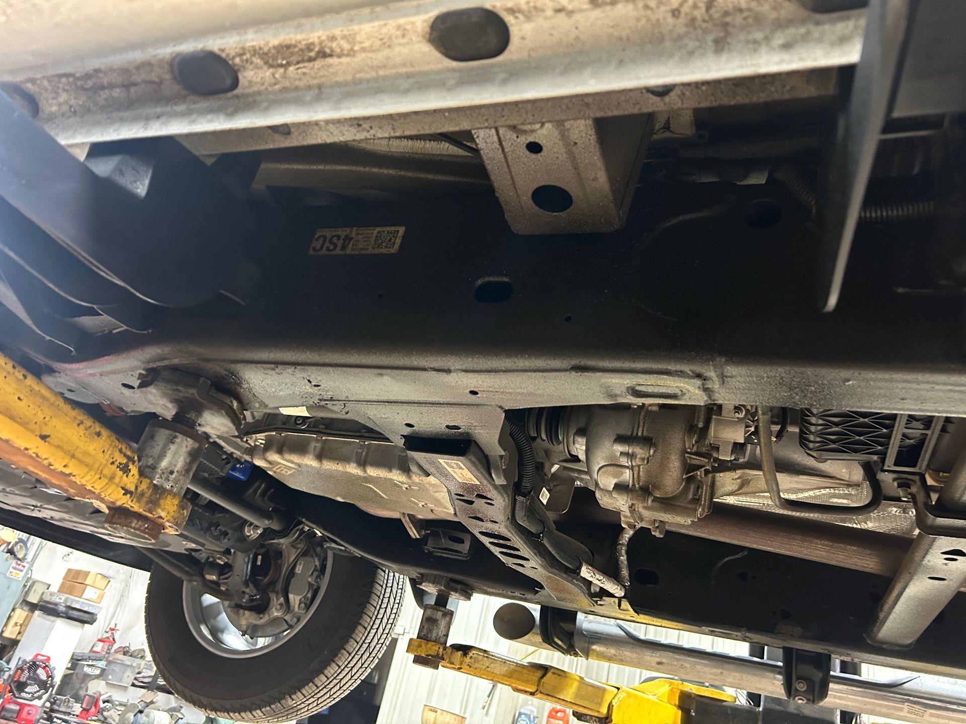 The underside of a car is sitting on a lift in a garage.