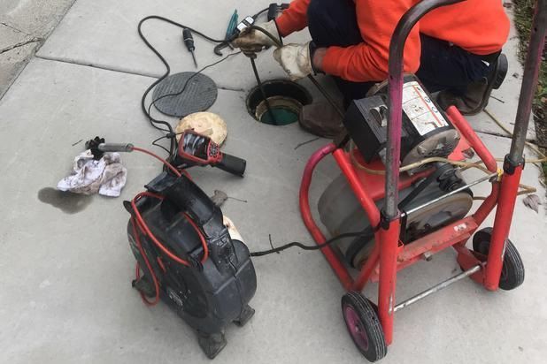 Person using equipment to work on a manhole, with tools and a machine on a concrete surface.