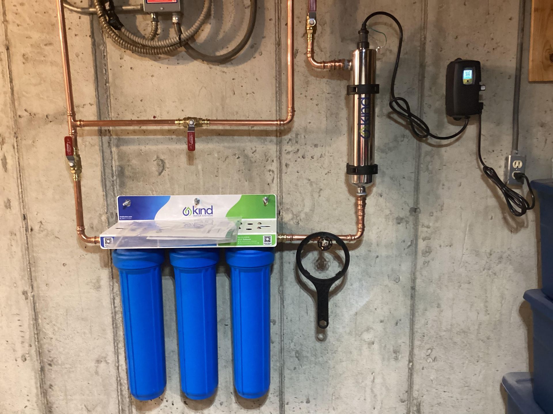 Water filtration system with blue filters, copper pipes, and a UV sterilizer installed on a concrete wall.