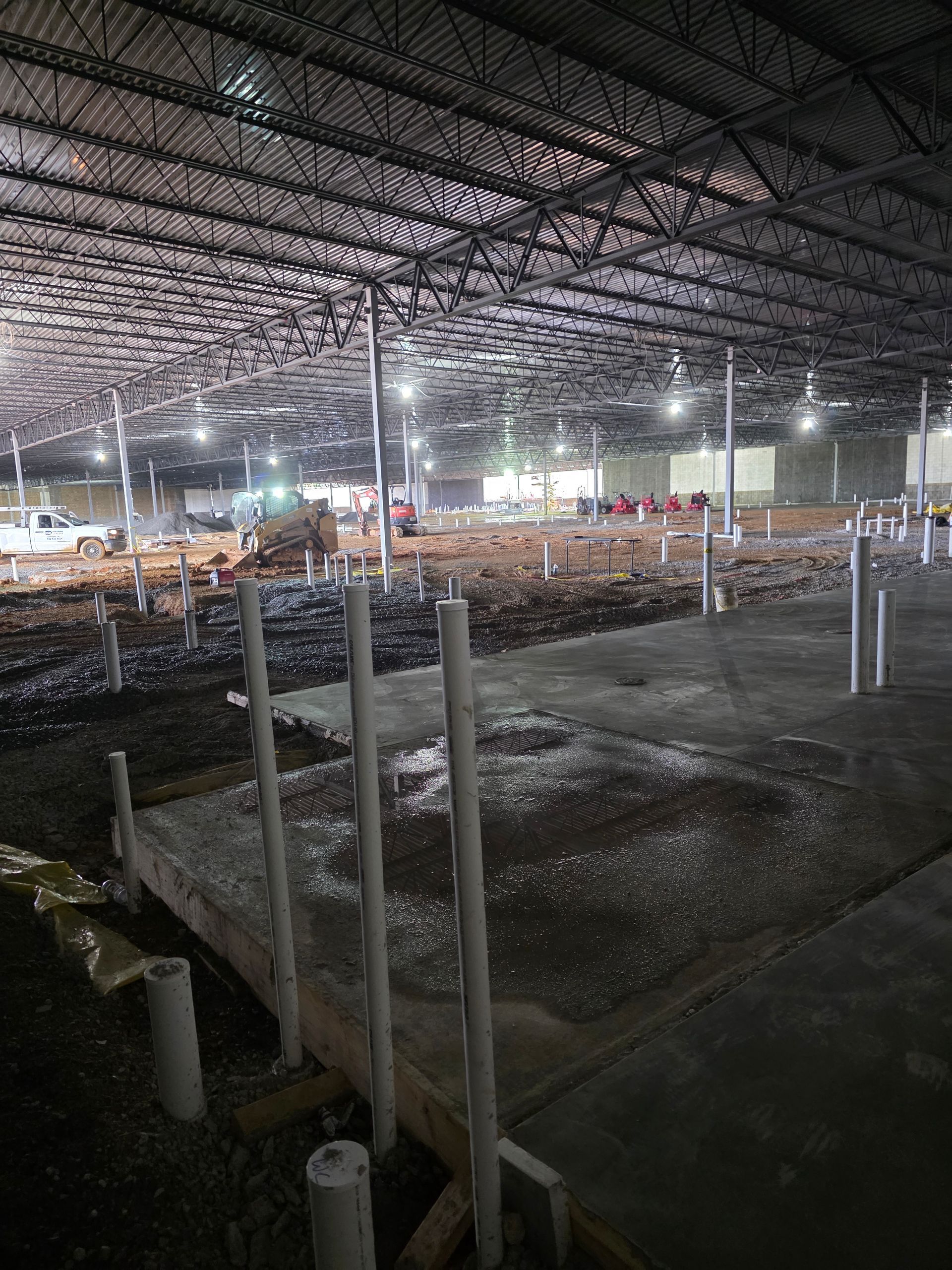 Inside of a large, unfinished building with concrete floor and exposed steel beams overhead.