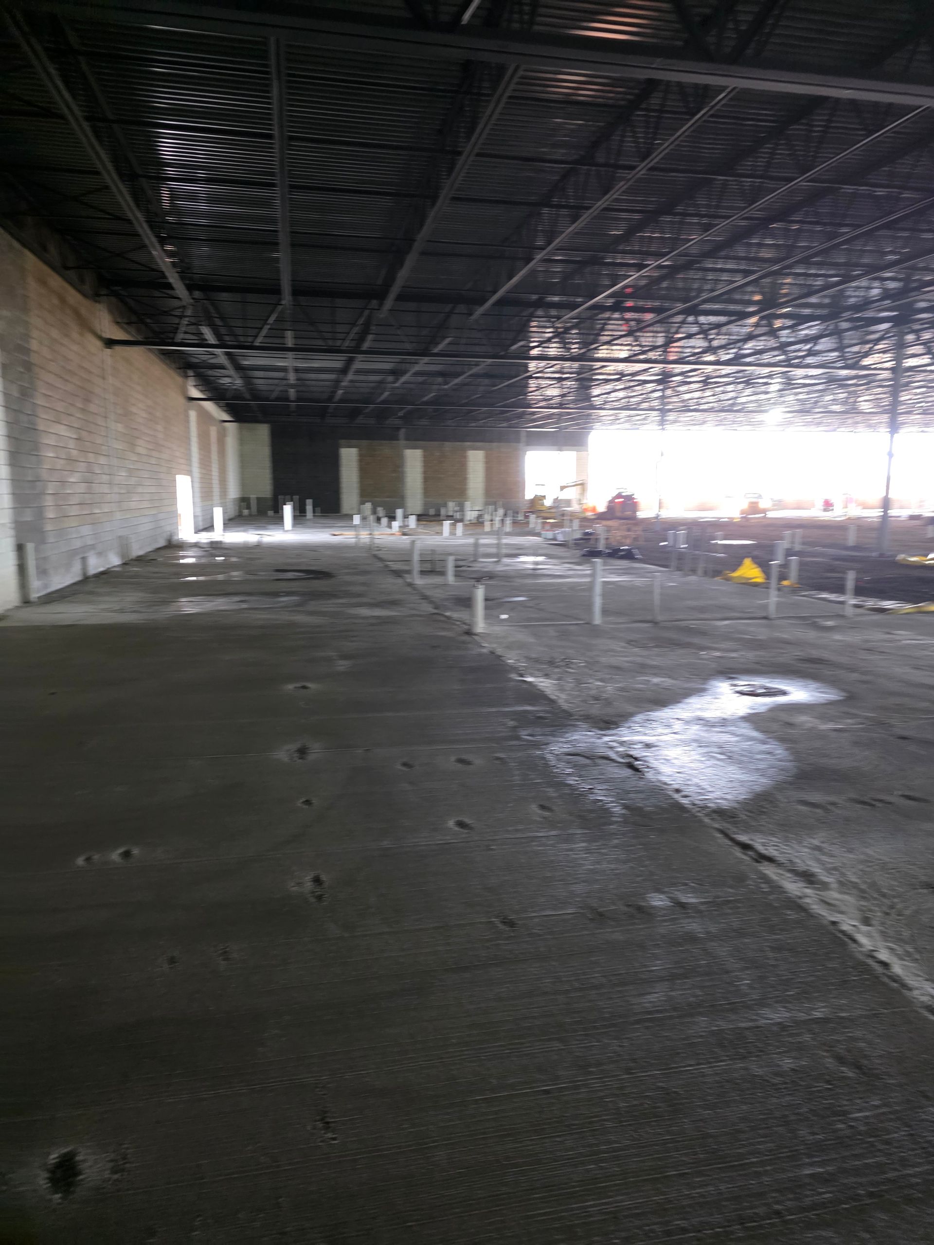 Interior view of a building under construction, showing a concrete floor and exposed ceiling supports.