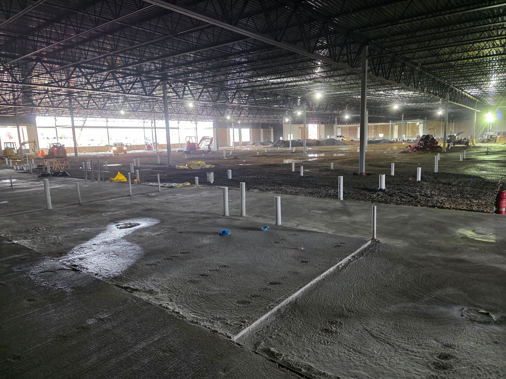 Large unfinished interior with concrete floor, metal beams, pipes, and construction debris.