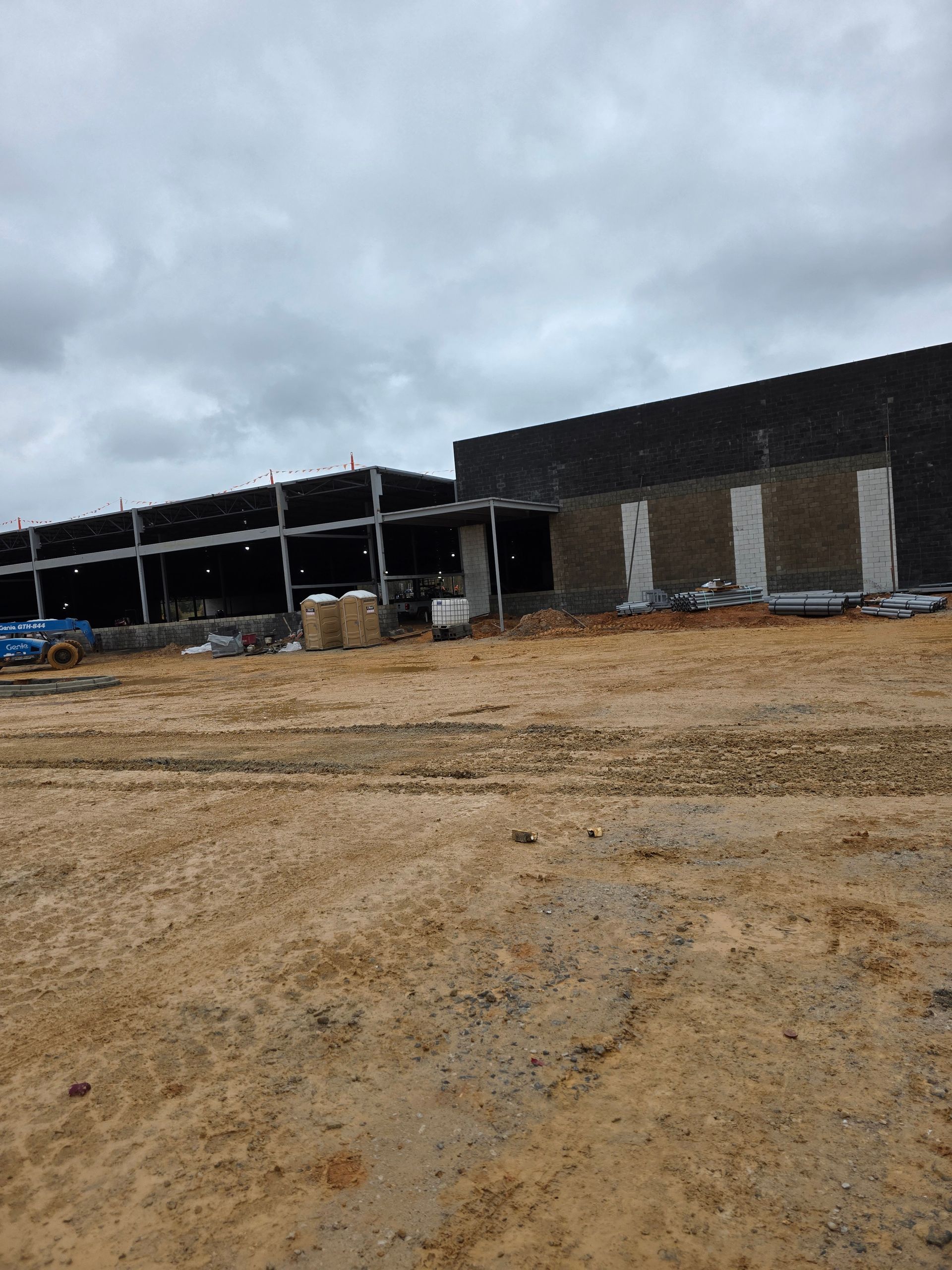 Construction site with partially built buildings under a cloudy sky. Brown dirt and concrete.