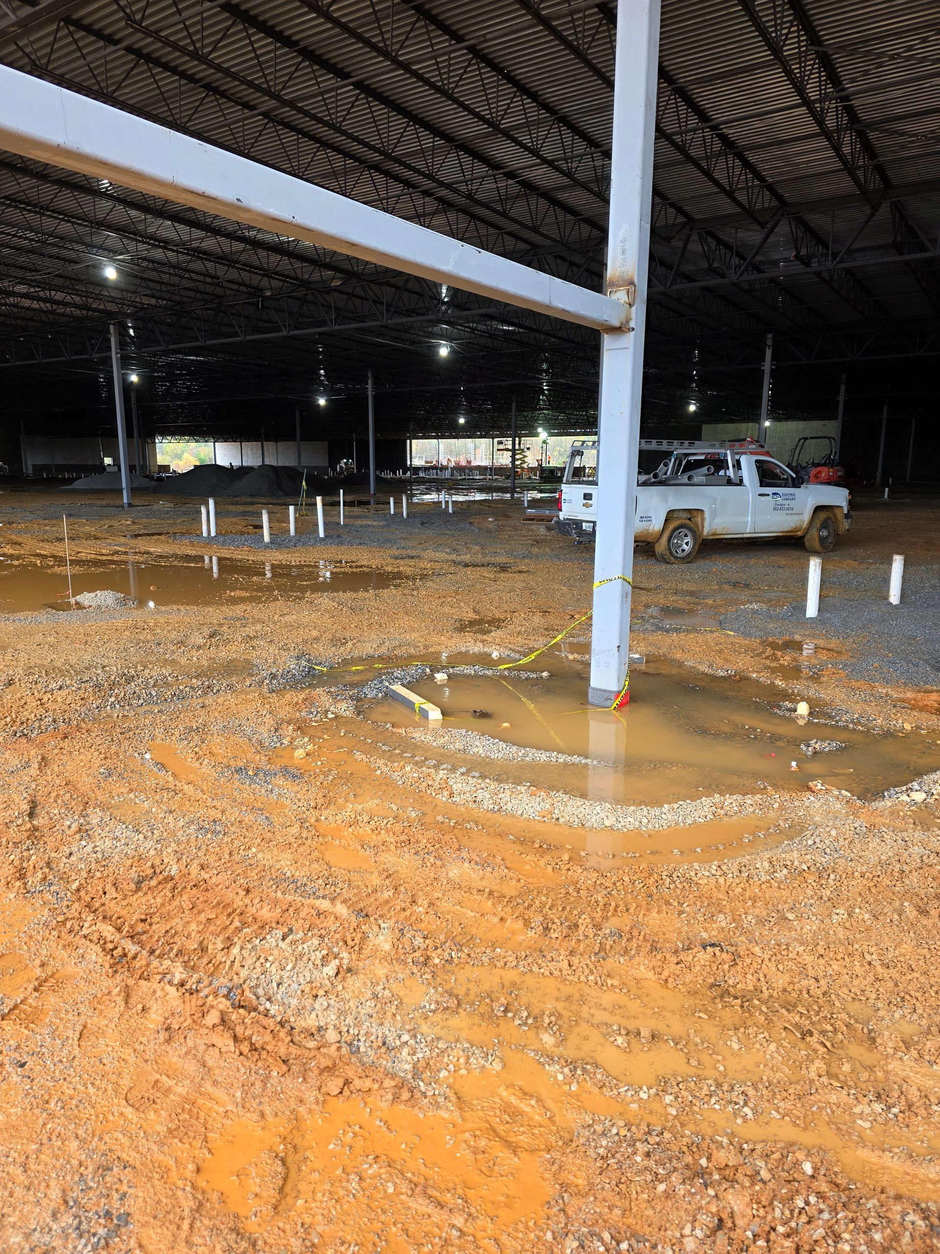 Flooded construction site with standing water and exposed soil. White truck parked in the background.