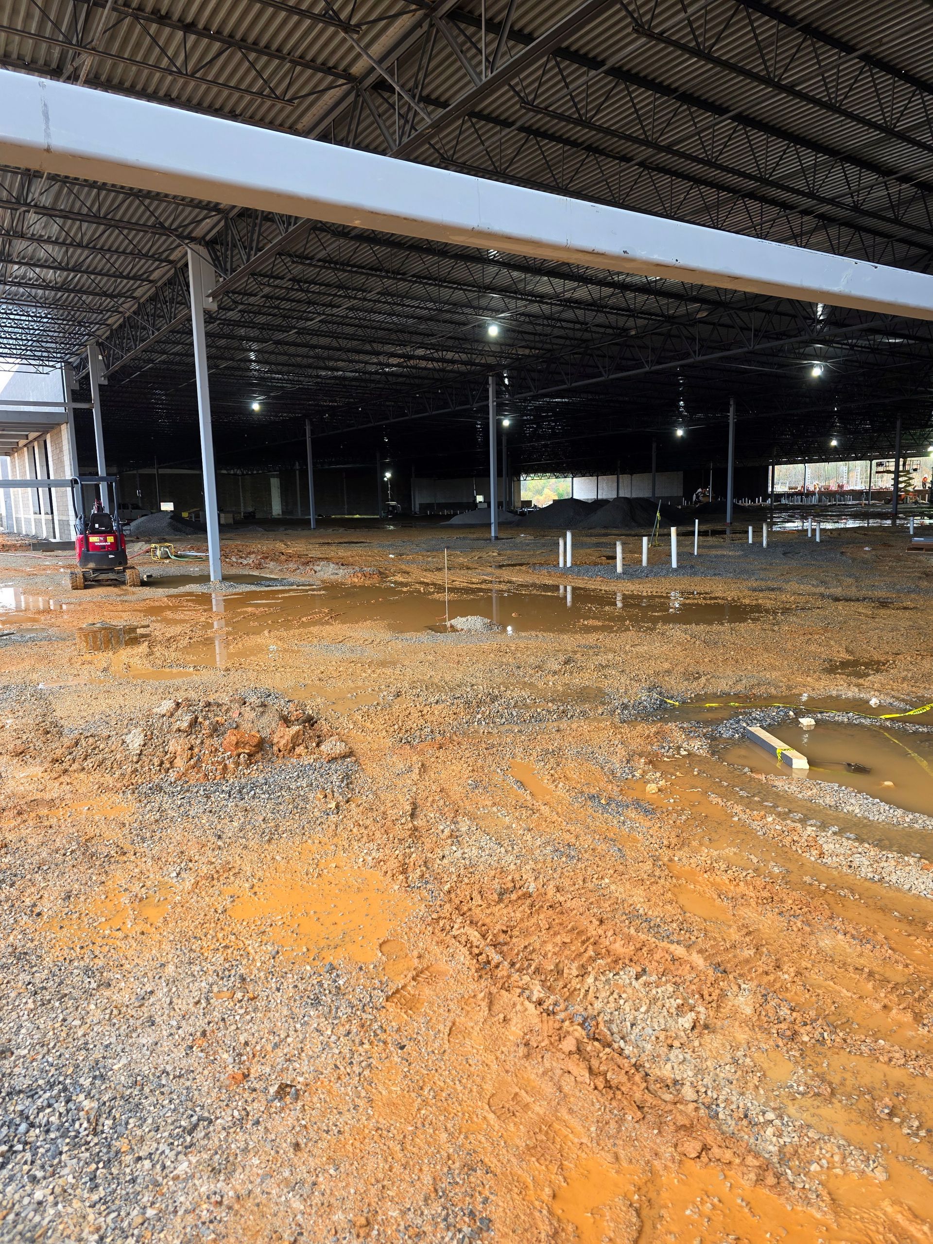 Interior of unfinished construction site; dirt floor, metal beams, and plumbing visible.
