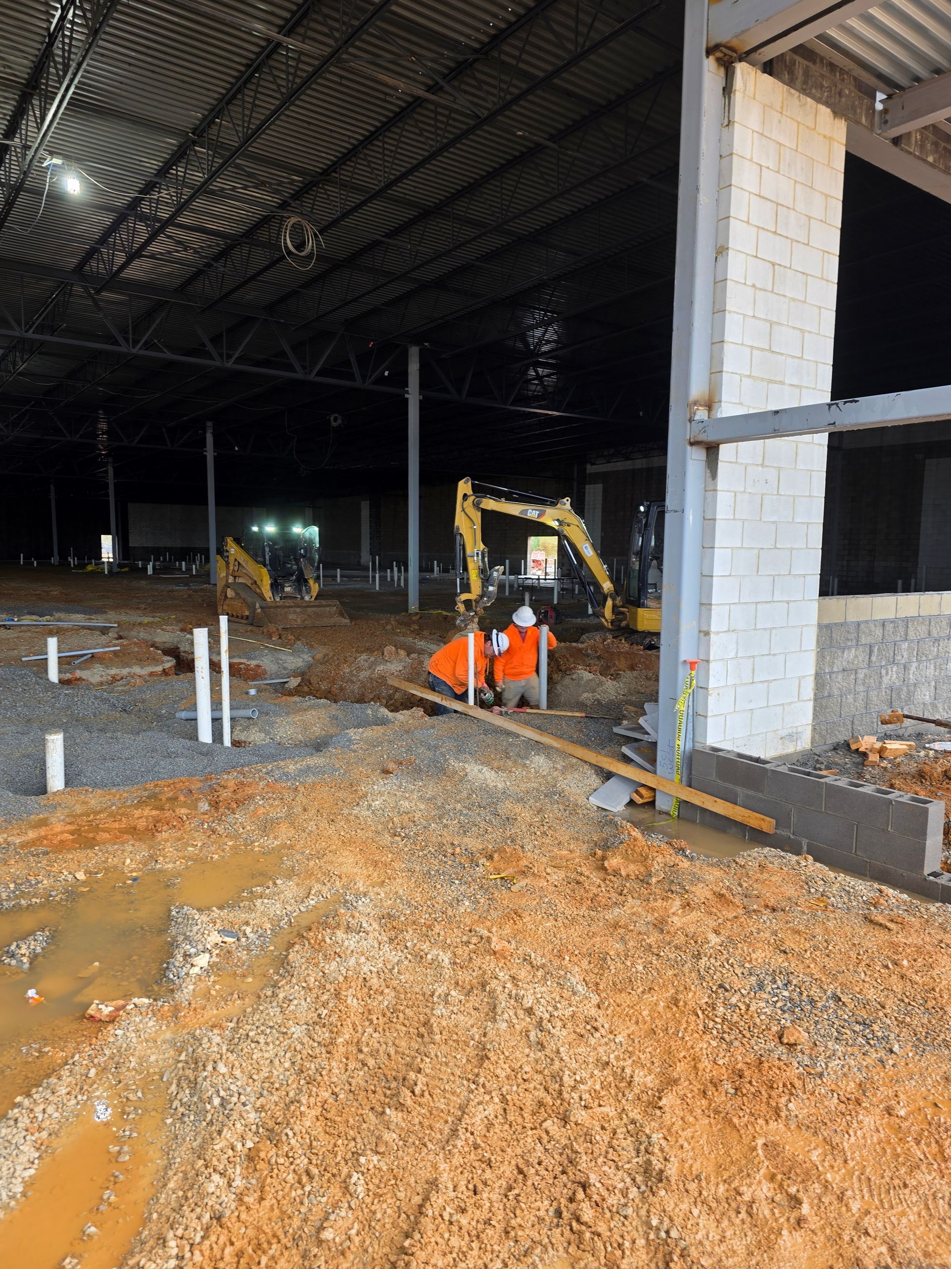 Construction site at night.  Excavator and worker near large white column,  digging in mud and dirt.