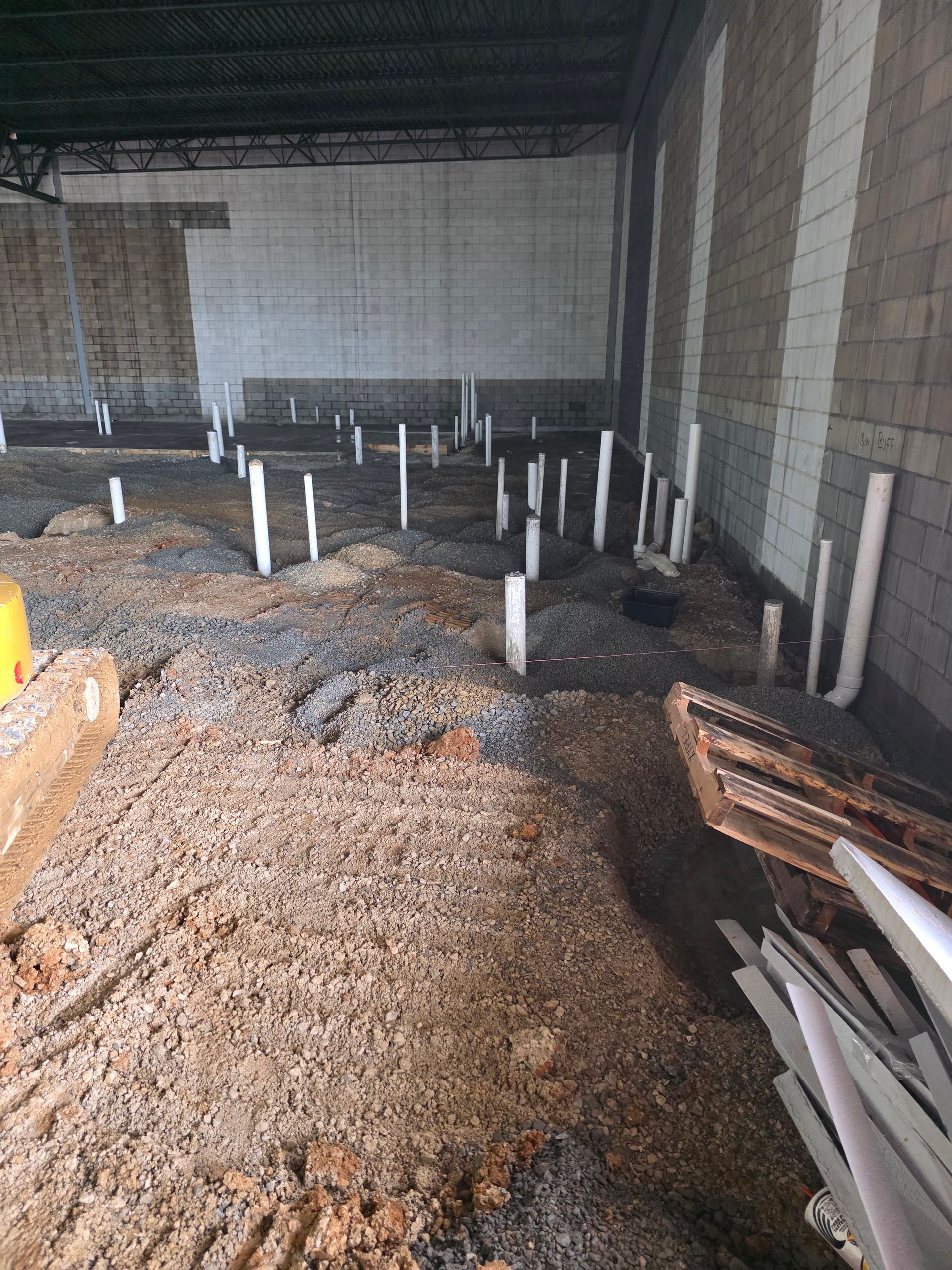 Interior construction site with plumbing pipes rising from gravel floor, next to cinder block walls.