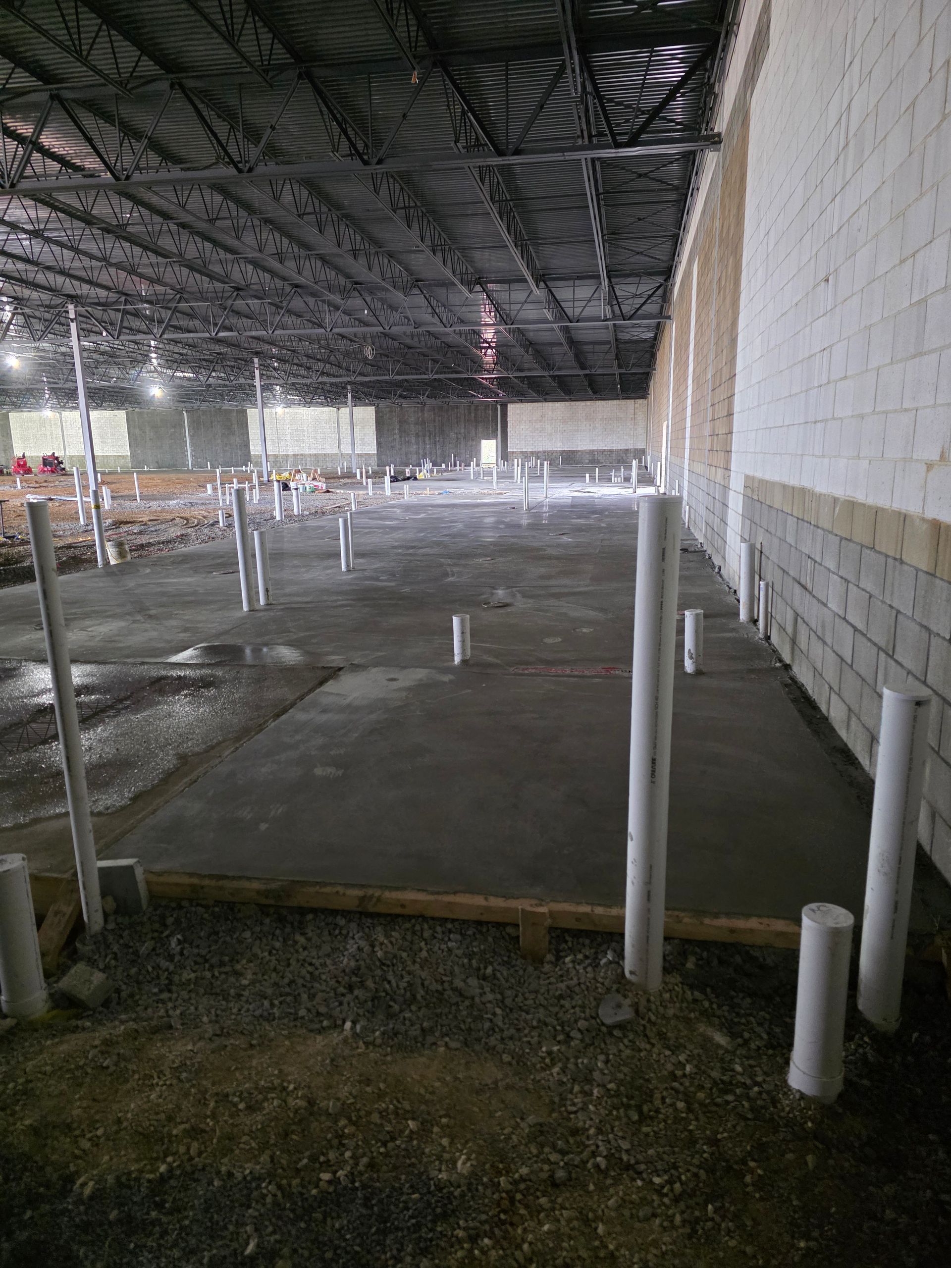 Construction site with a concrete floor, plumbing pipes, and brick wall. Black ceiling and open space.
