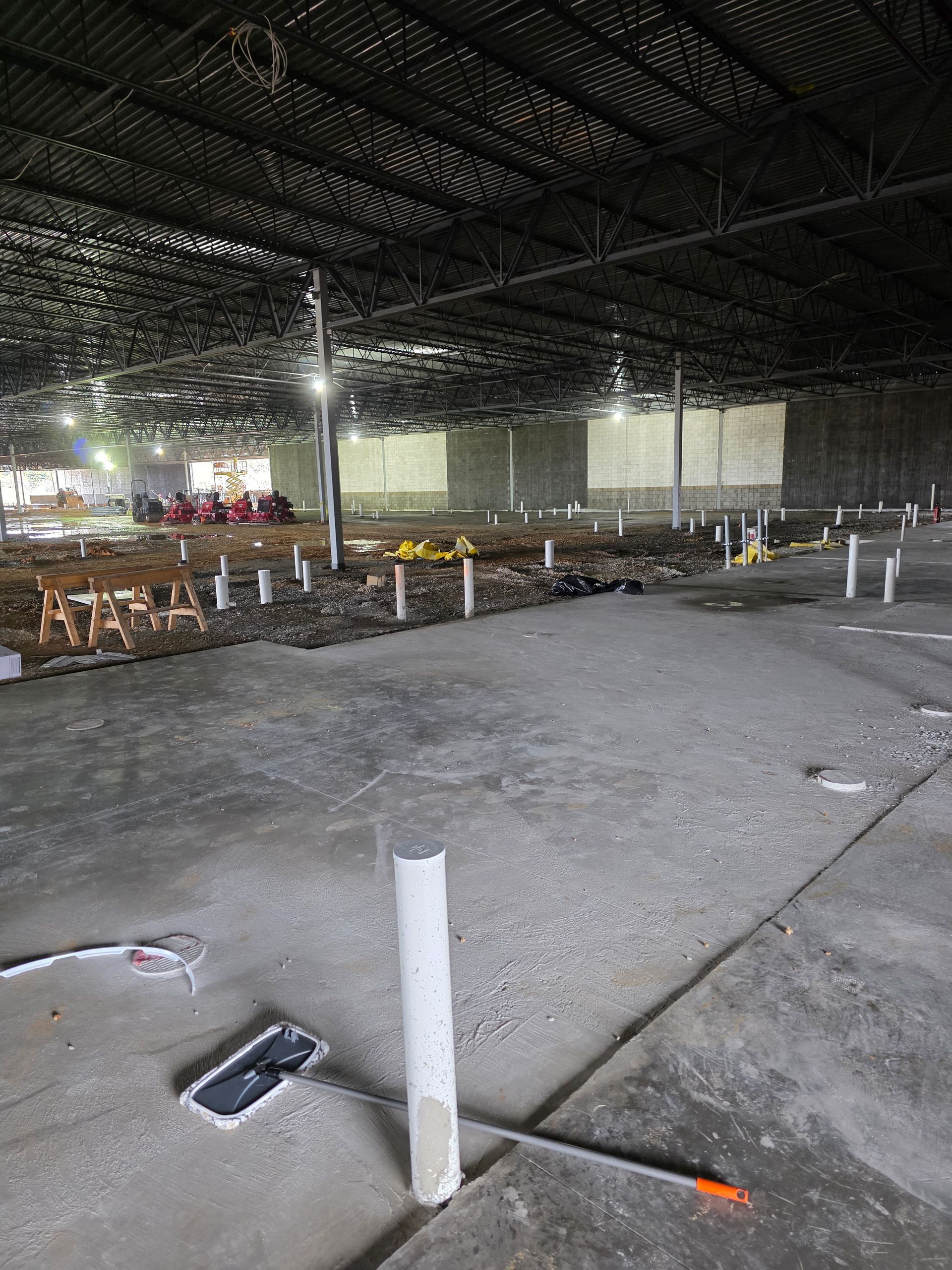 Interior of a large, unfinished industrial space with concrete floor, exposed pipes, and dark ceiling.
