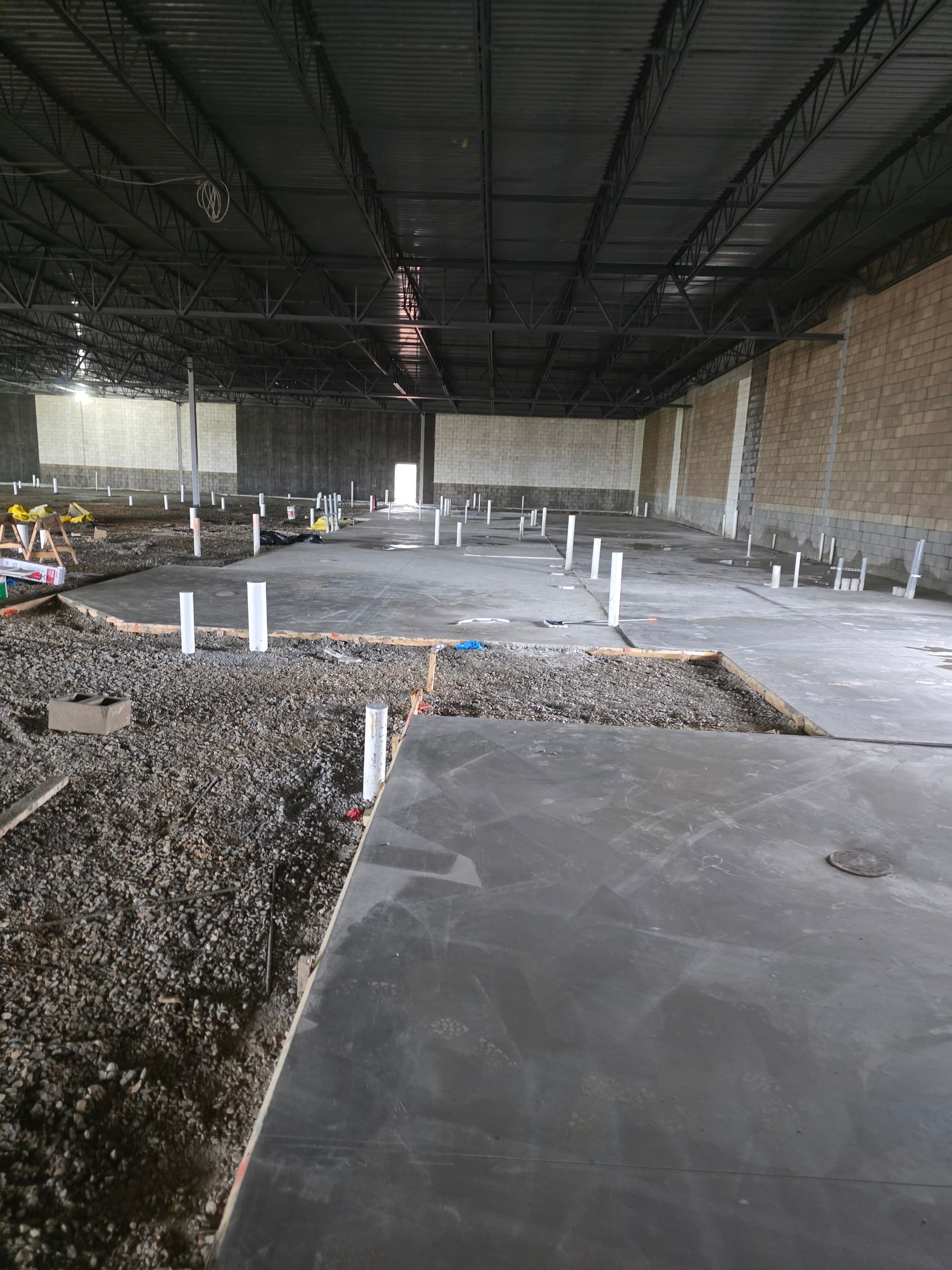 Interior of a large unfinished building with concrete flooring, plumbing pipes, and exposed ceiling