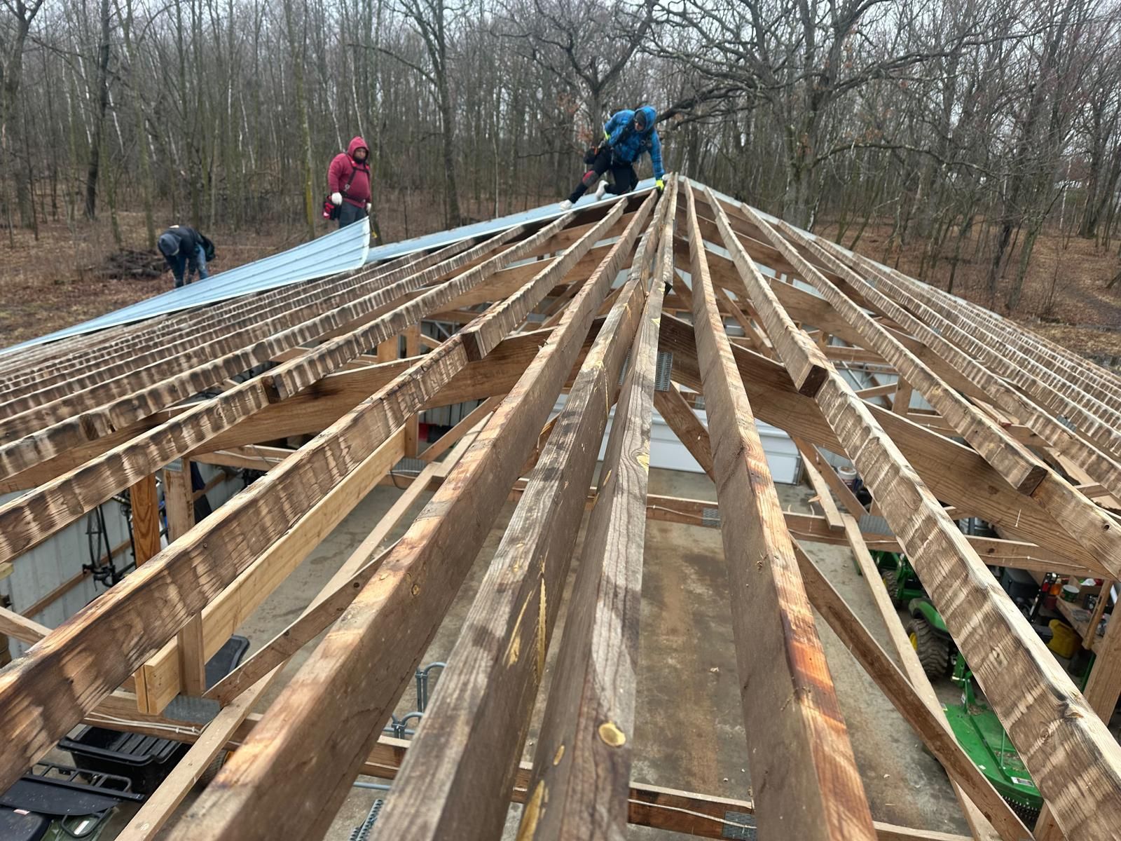 Workers installing metal roofing on a wooden structure; set in a wooded area.