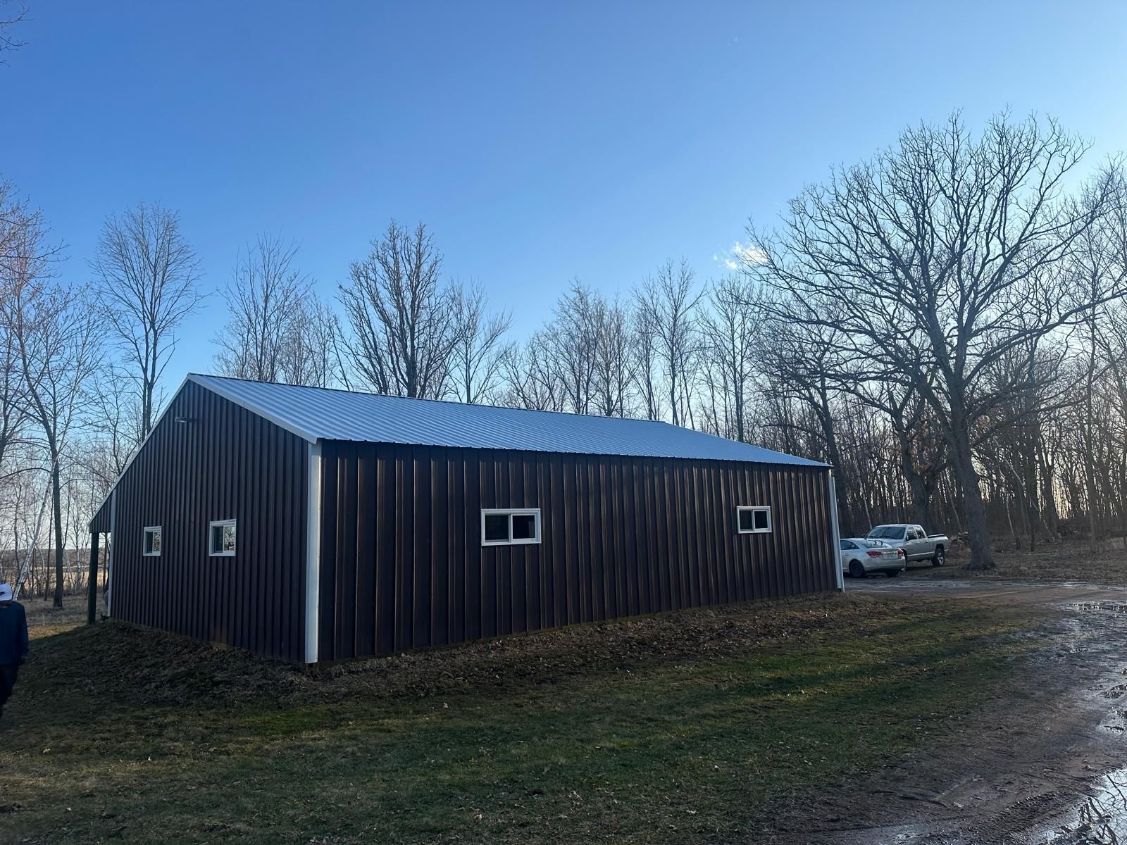 Brown metal shed with white trim and a blue corrugated metal roof. Located on grassy land near bare trees.