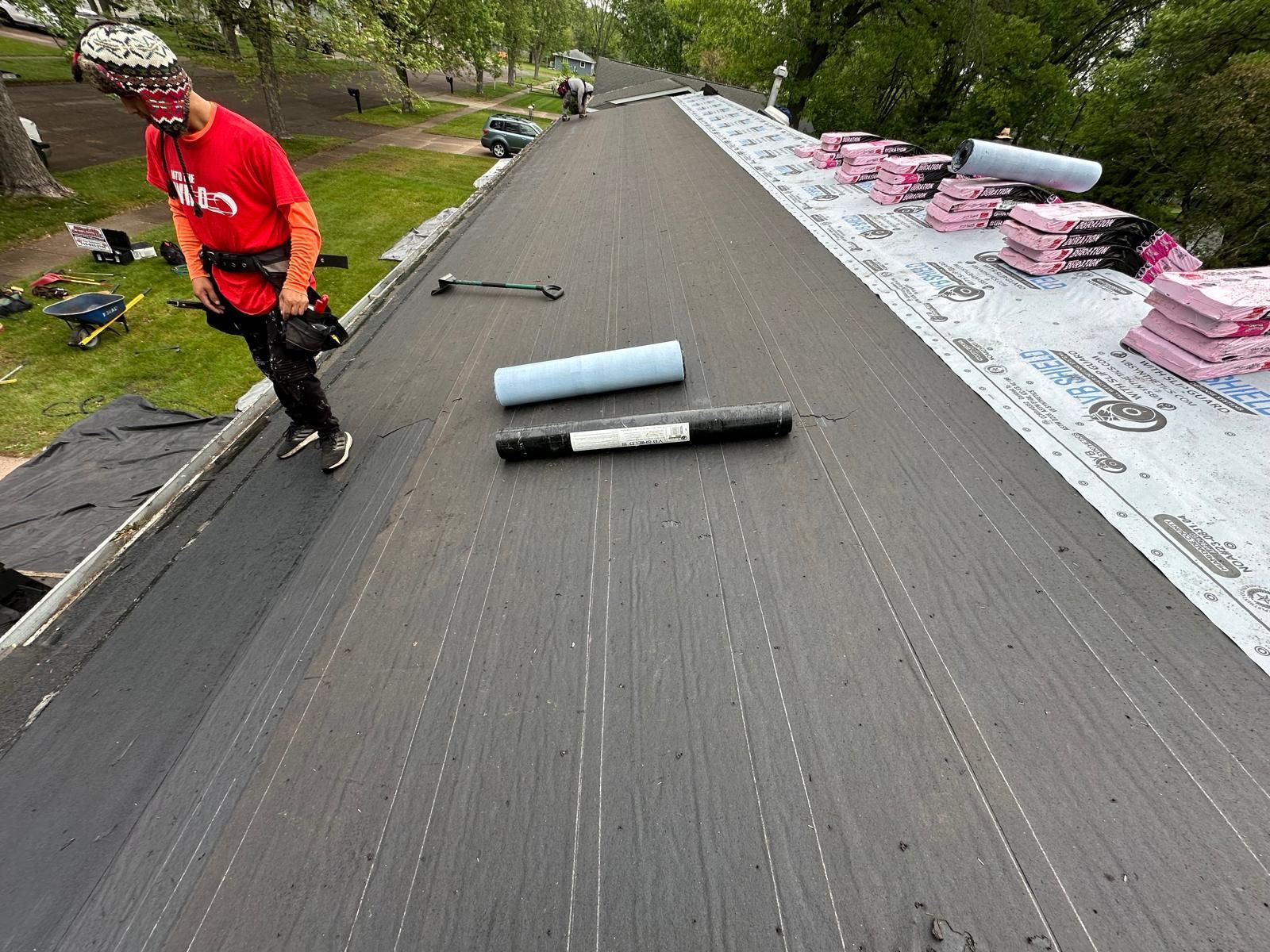 Roofer on a roof, installing roofing underlayment. The roof is black.