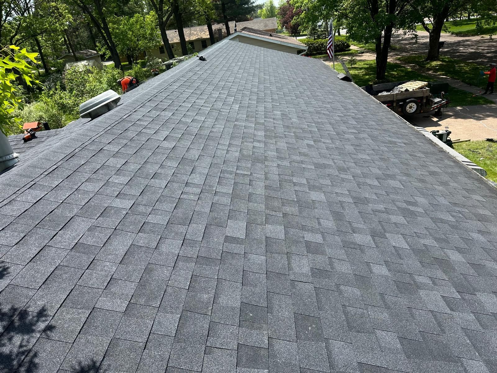 Dark gray asphalt shingle roof on a house, under a sunny sky.