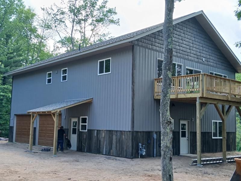 Two-story building with gray siding, wooden deck, and a person standing near a door.