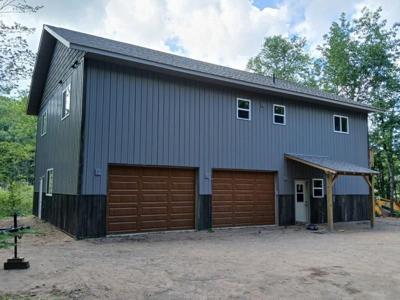 Two-story gray building with brown garage doors. Small covered entry. Set in a dirt lot, trees in background.