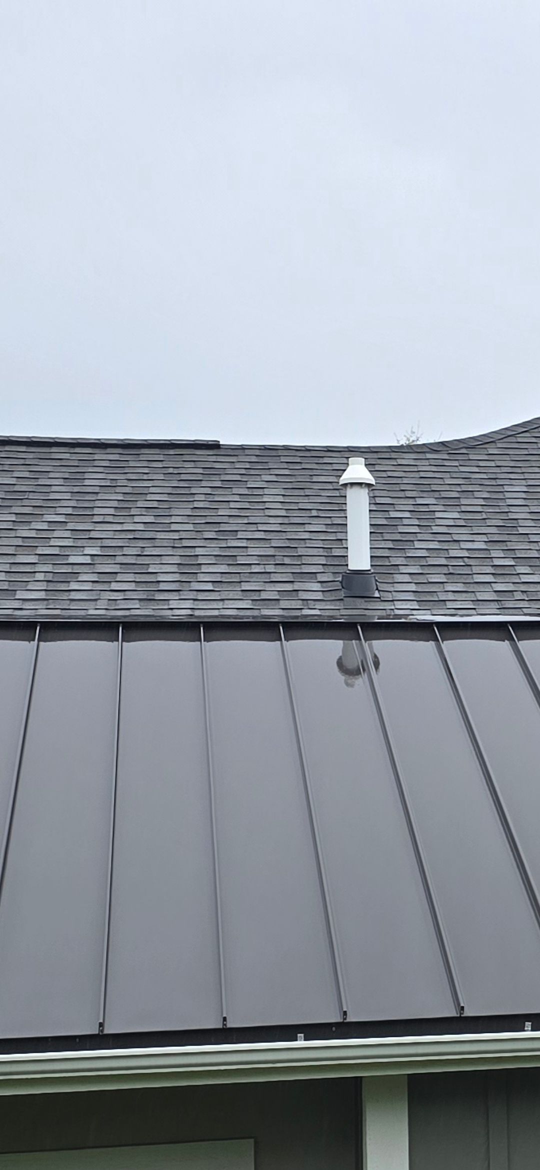 Metal roof with vent pipe against a cloudy sky.