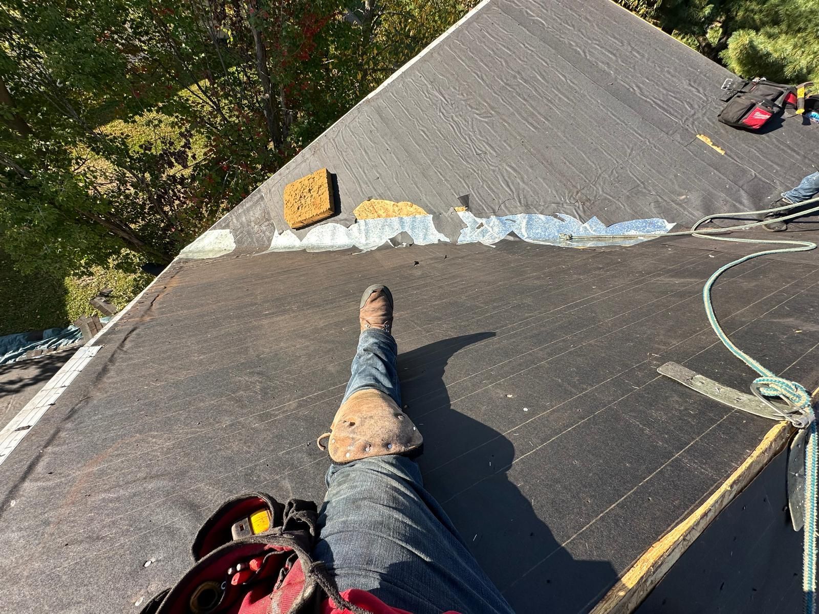 Person on a rooftop working on the roof's edge, wearing work boots and safety gear.