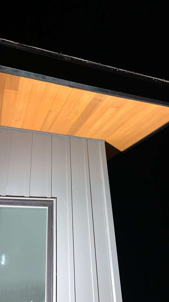 Corner of a building with wooden soffit and white siding. Dark sky.