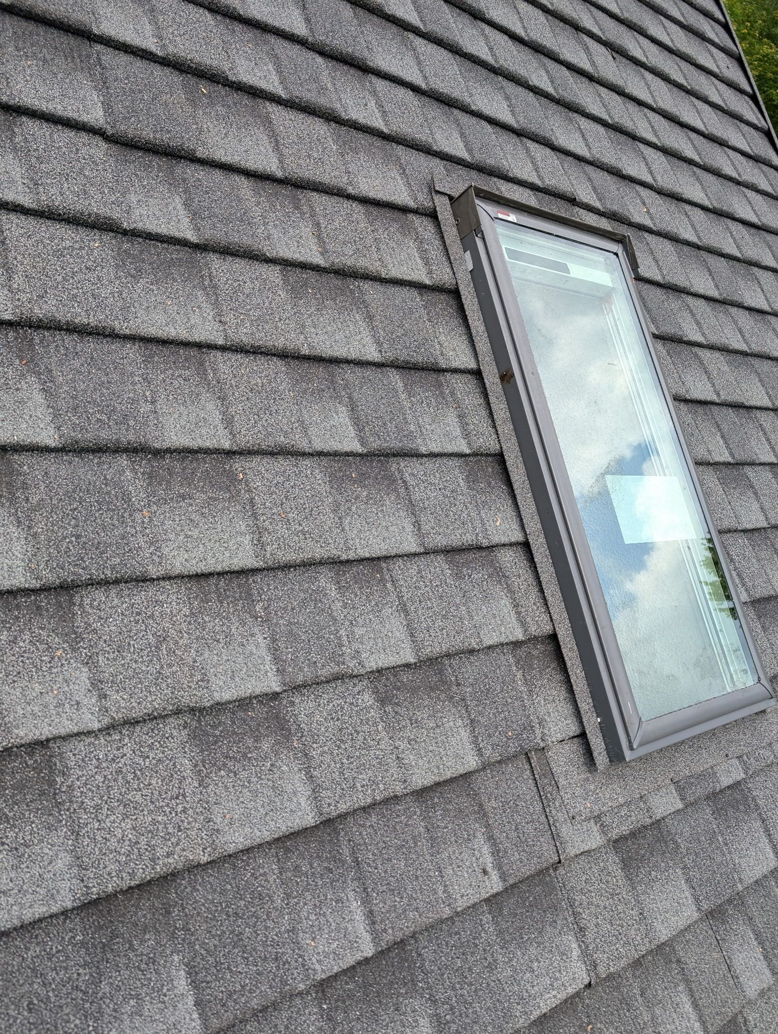 Gray shingle roof with a rectangular skylight. The sky is reflected in the skylight.