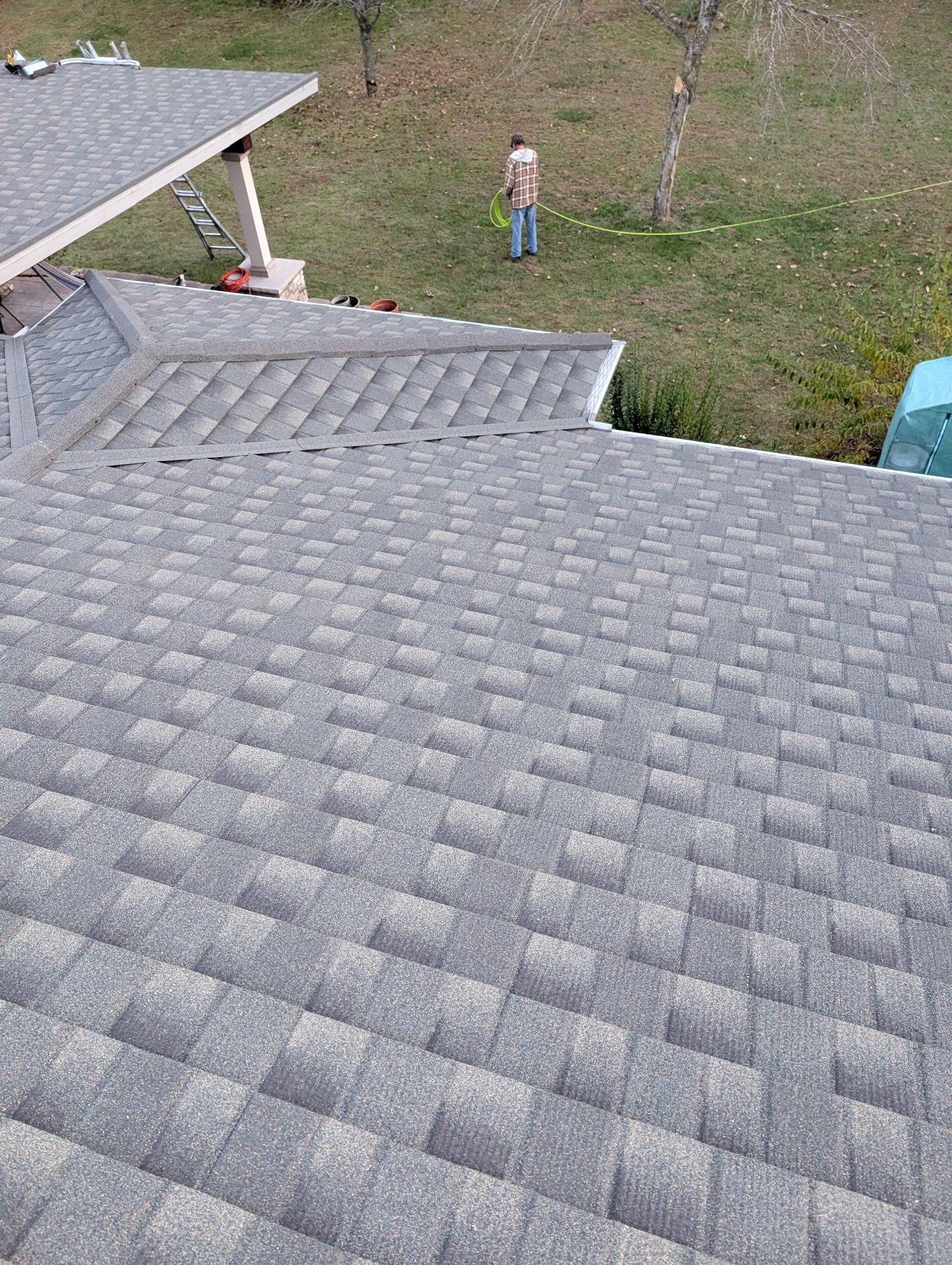 Gray asphalt shingle roof on a house, with a person standing in the grass below.