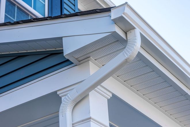 White gutters and downspout on a light blue house, against a clear sky.
