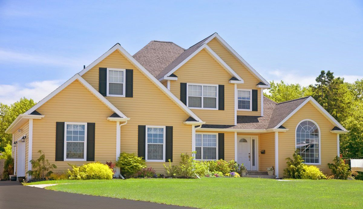 Yellow two-story house with black shutters, green lawn, and blue sky.