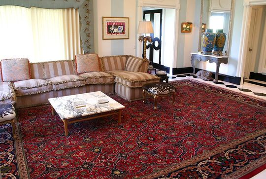 Living room with sectional sofa on a large red rug; marble coffee table, ornate details, and striped walls.