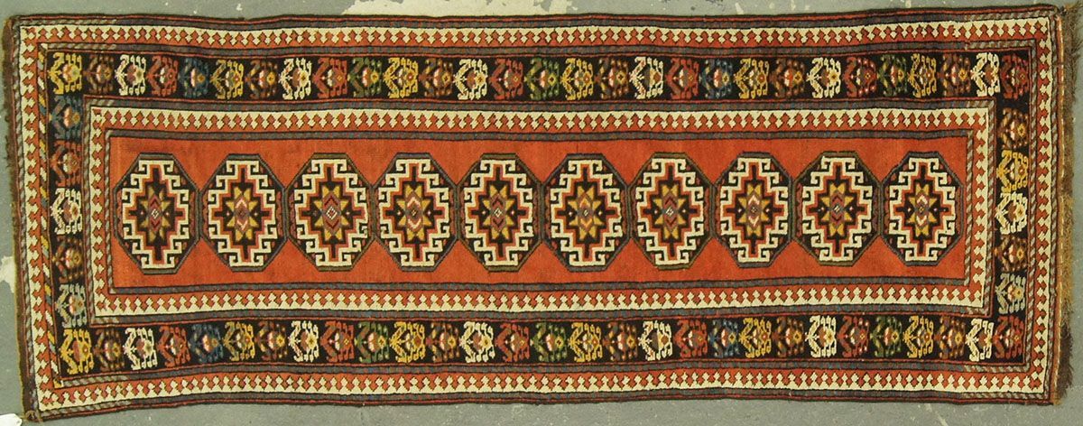 Rectangular rug with a central panel of repeating geometric motifs in orange, brown, and ivory