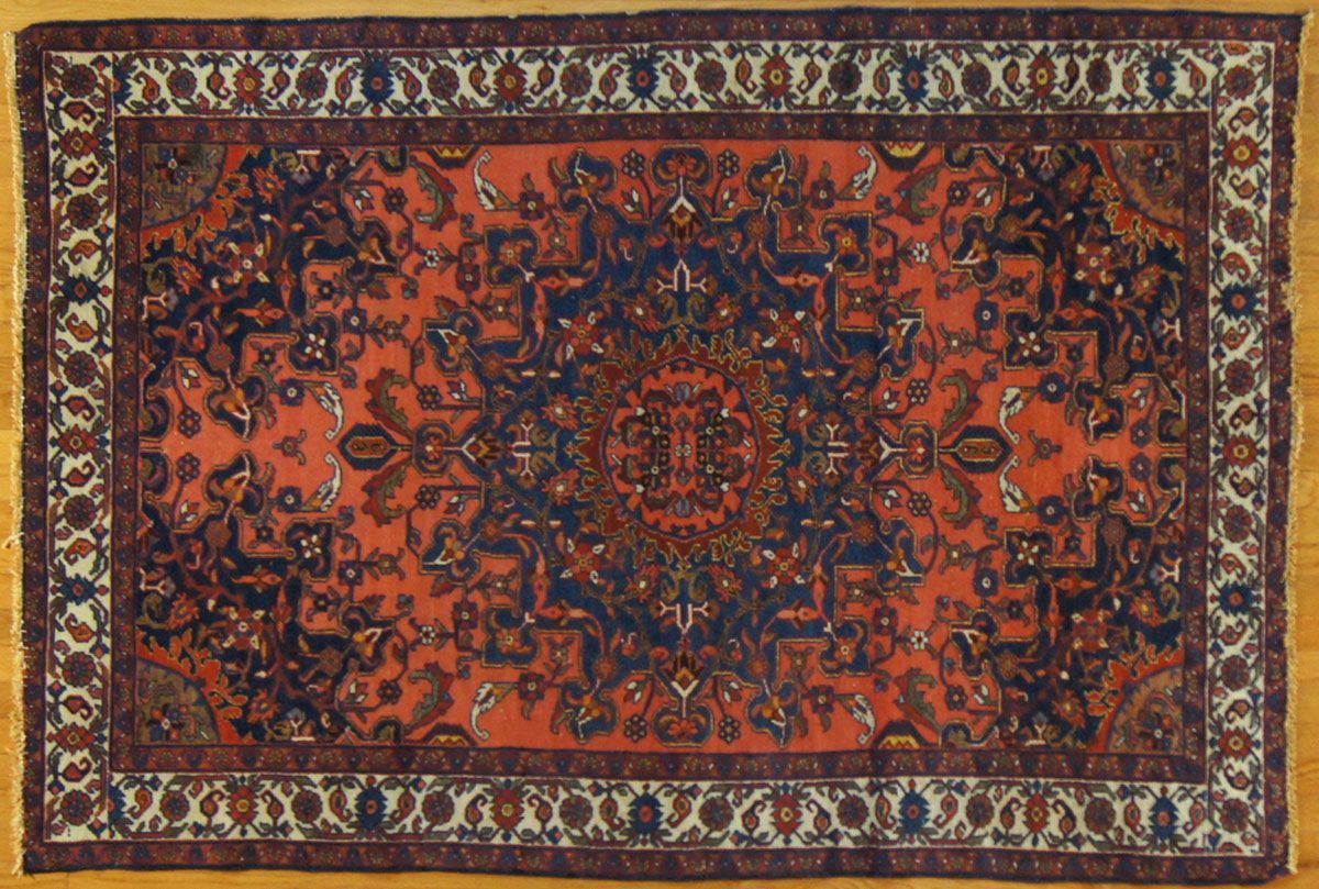 Oriental rug with a red-orange field, intricate dark blue central design, and ivory border with floral motifs