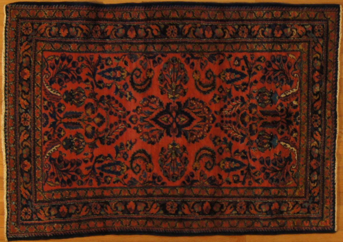 Red and navy oriental rug with intricate floral pattern on a wooden floor