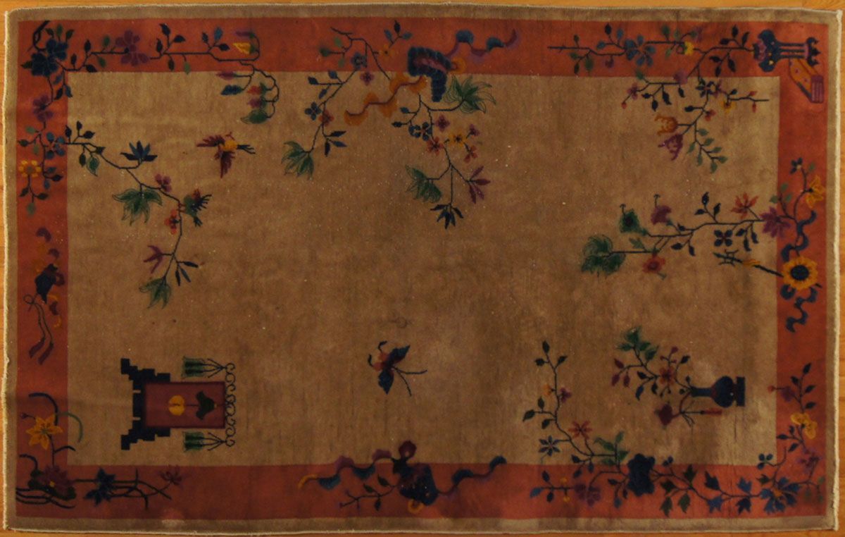 Oriental rug with floral and bird designs, bordered in red on a wood floor