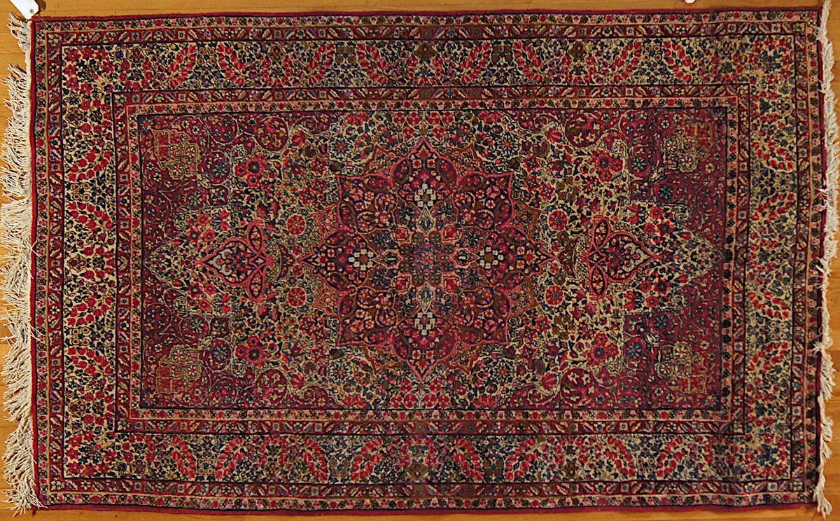Red and green patterned rug with fringe on a wooden floor