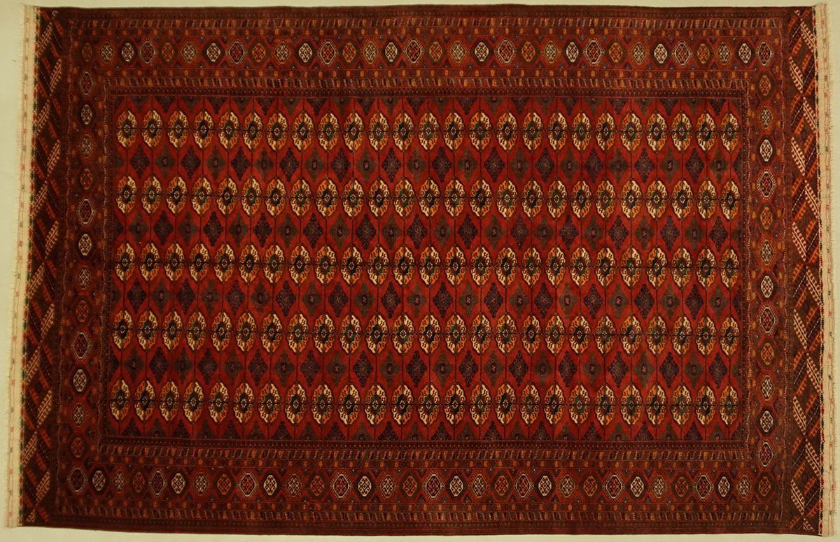 Red rectangular rug with repeating diamond patterns, intricate border, and fringe