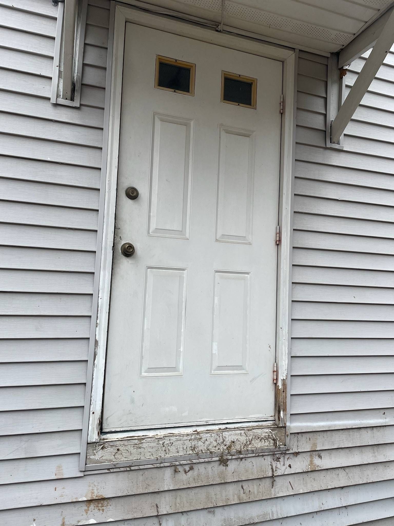 White door with four panels, two small top windows. Building exterior with peeling paint.