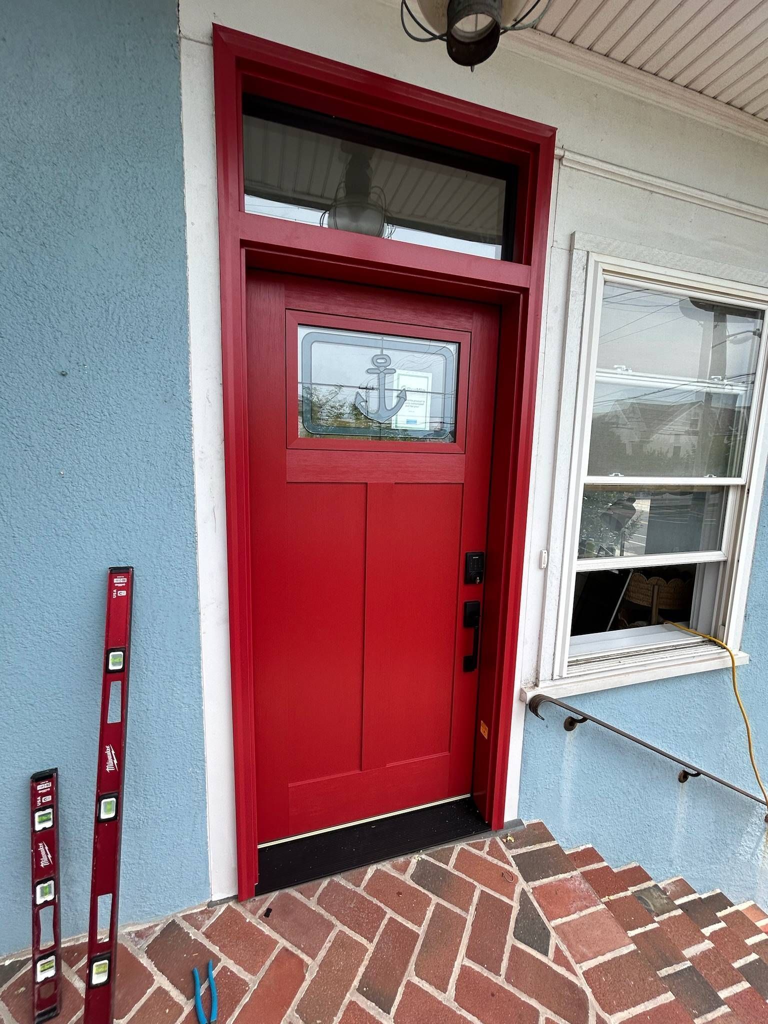 Red front door with a window and trim, set in a blue and white building, brick steps, and a level.
