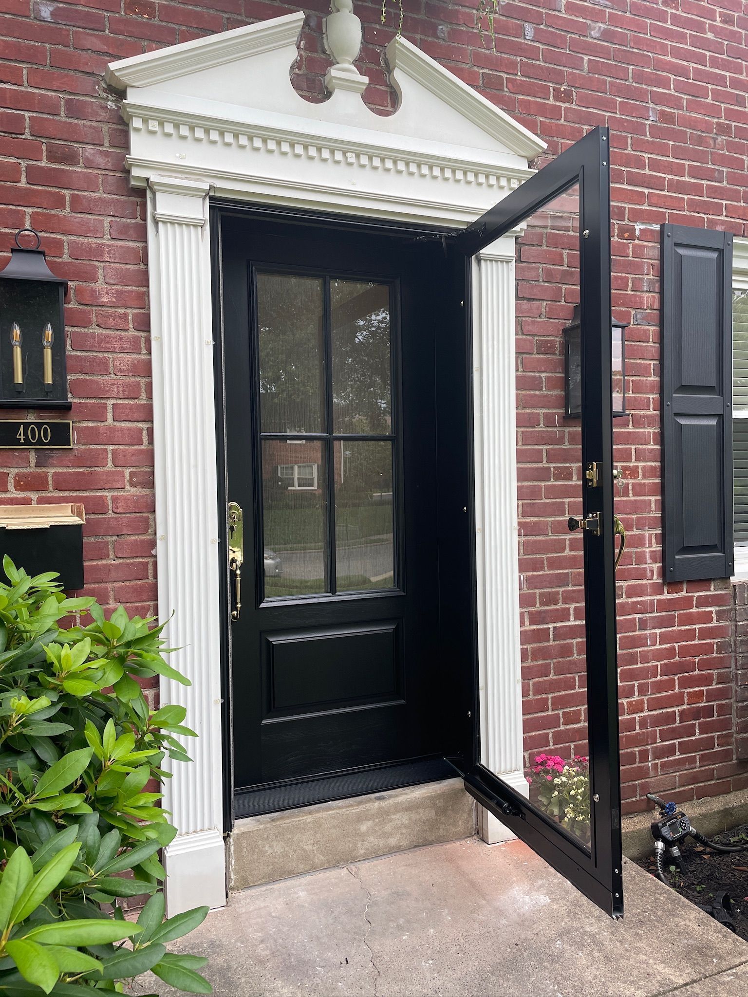 Black front door with open screen door, brick facade, white trim.