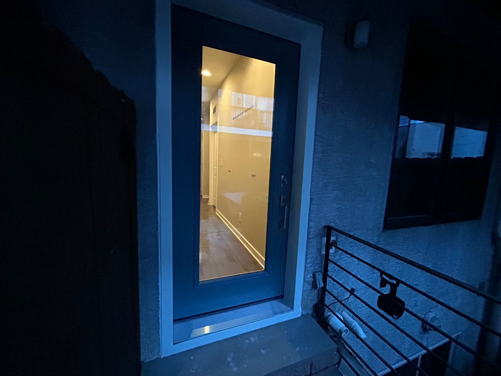 Exterior view of a blue door with a window, leading to a well-lit hallway.