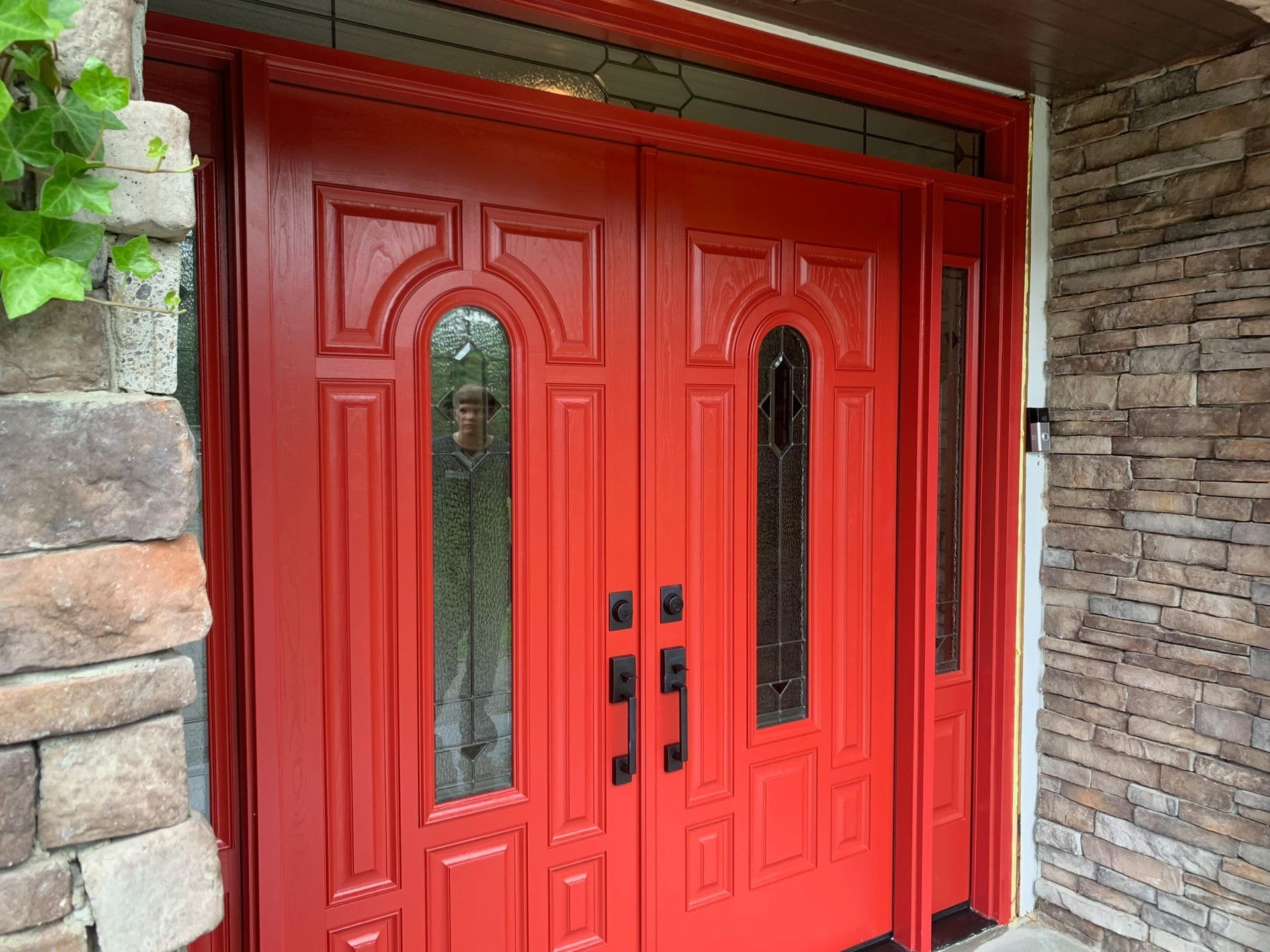 Red double doors with glass panels and black handles; exterior of a building with stone and brick details.